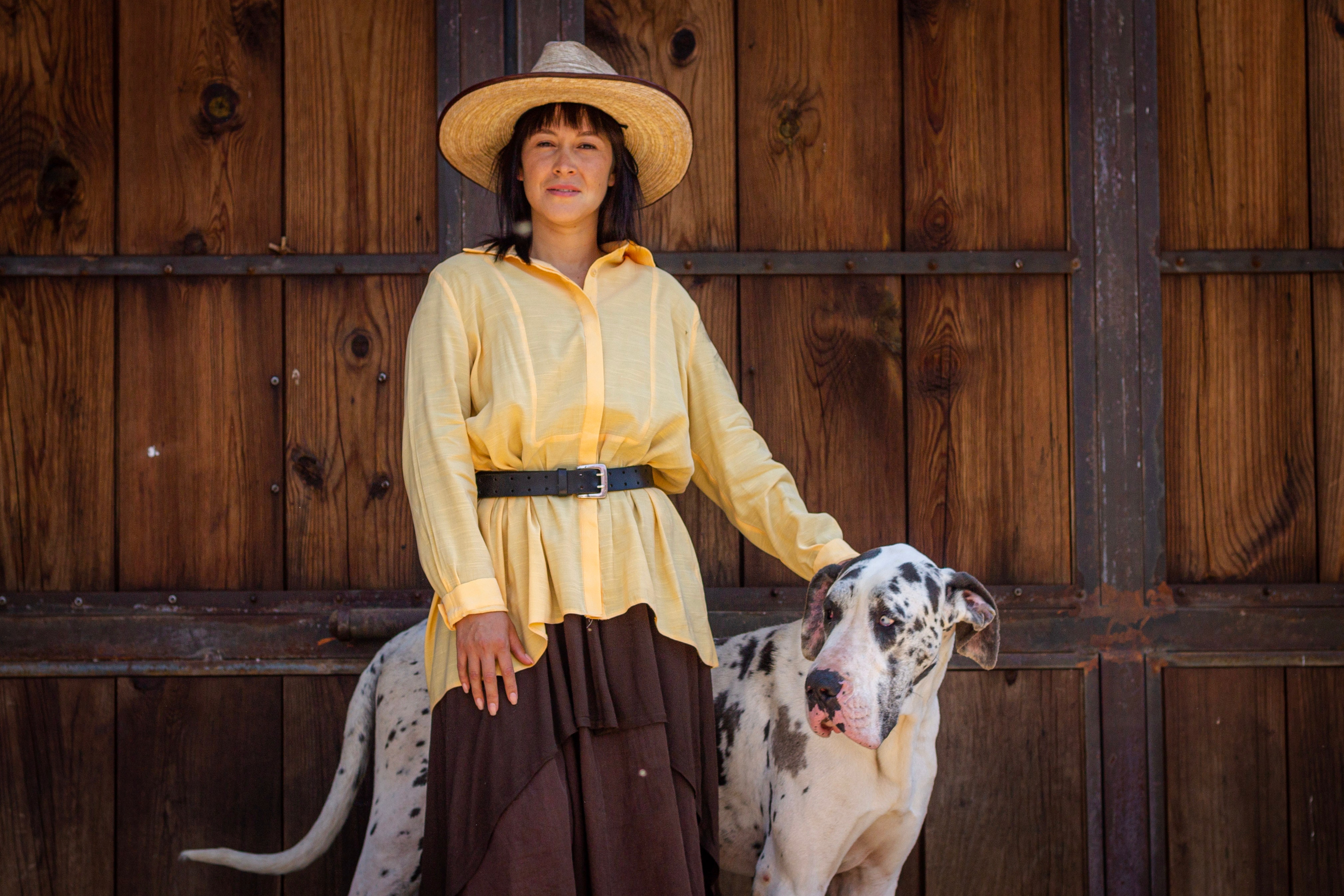 harlequin great dane standing next to a woman in a brown skirt and a yellow shirt and hat 